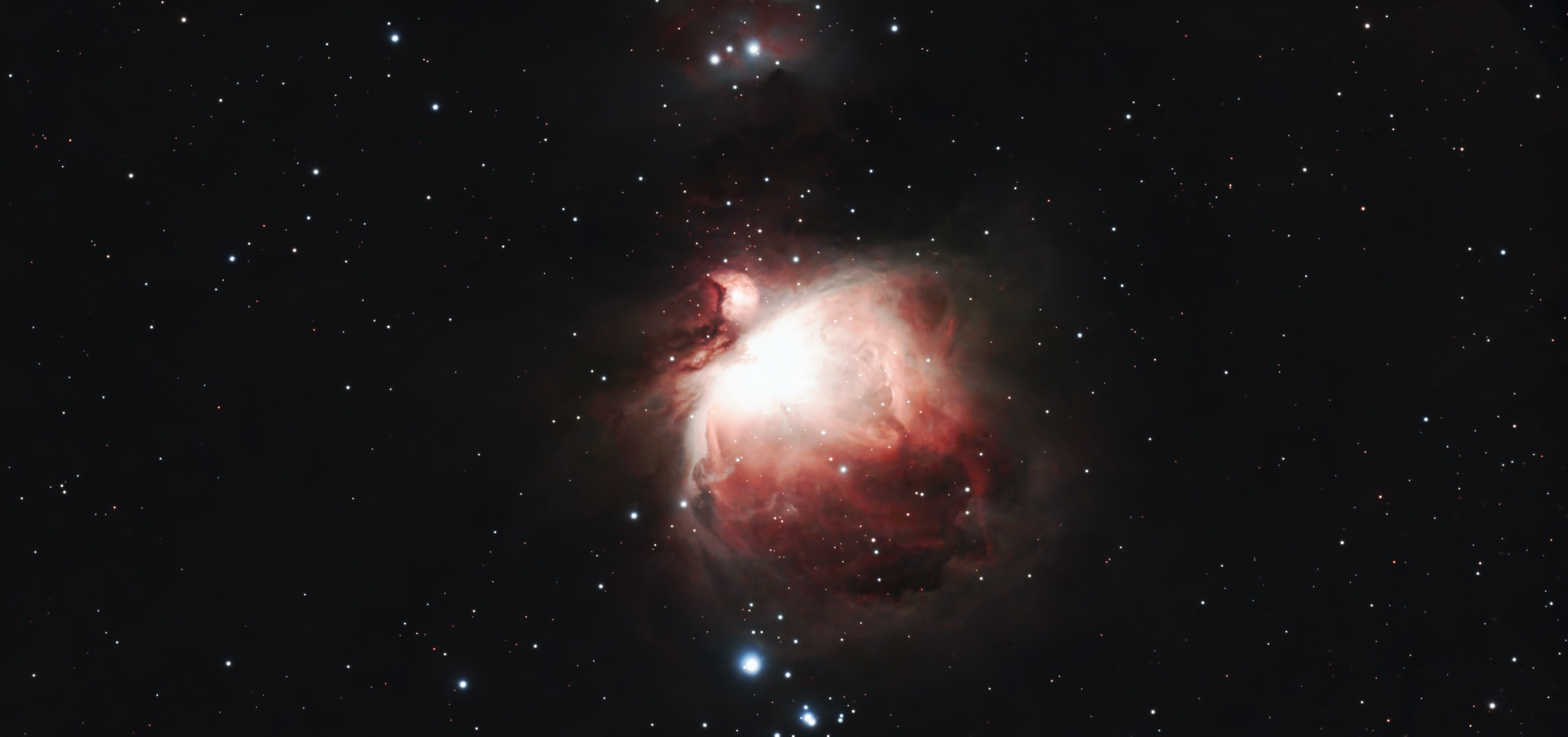 猎户座大星云（M42）深空摄影图像，呈现出核心明亮的发光气体云与外围伸展的红色电离氢云气以及复杂的暗尘埃带。